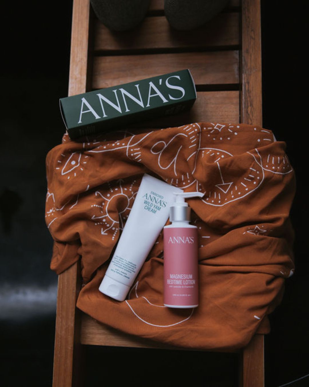 ANNA'S skincare products on a brown fabric with a wooden ladder background
